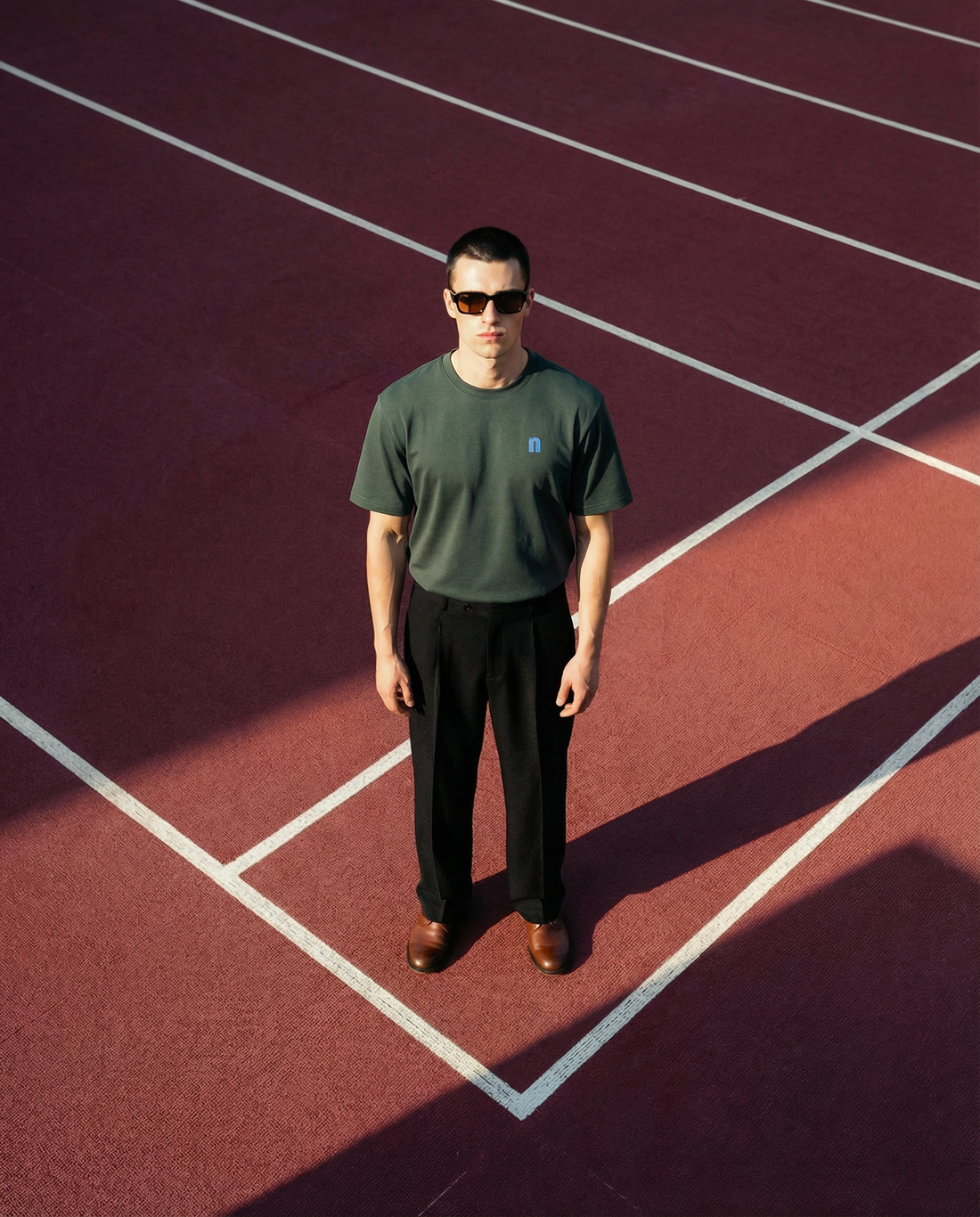 A model wearing Normal Standard Entry classic t-shirt standing at the edge of running track posing for the photo.
