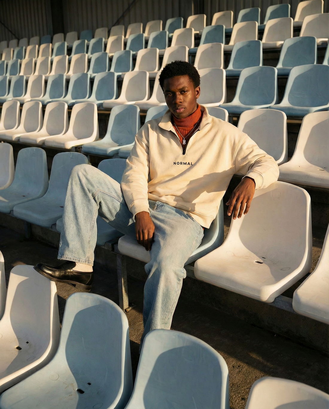 Model sitting in a stadium wearing normal standard sweatshirt.
