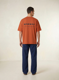 Sinopia | Person wearing an orange t-shirt with 'NORMAL STANDARD' text on a plain background