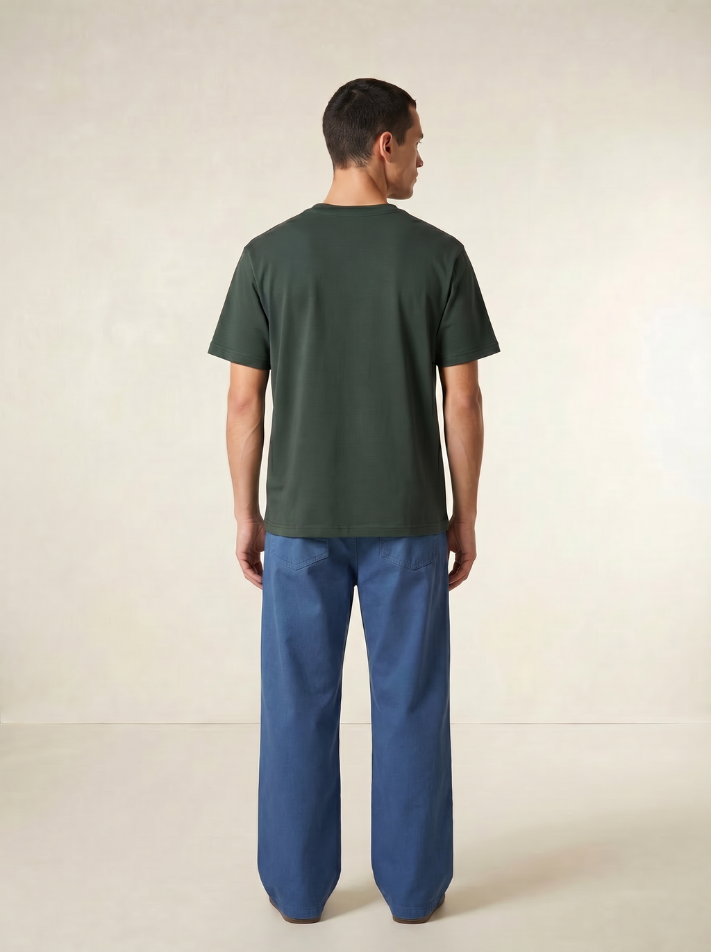 Man wearing a green t-shirt and blue pants on a beige background