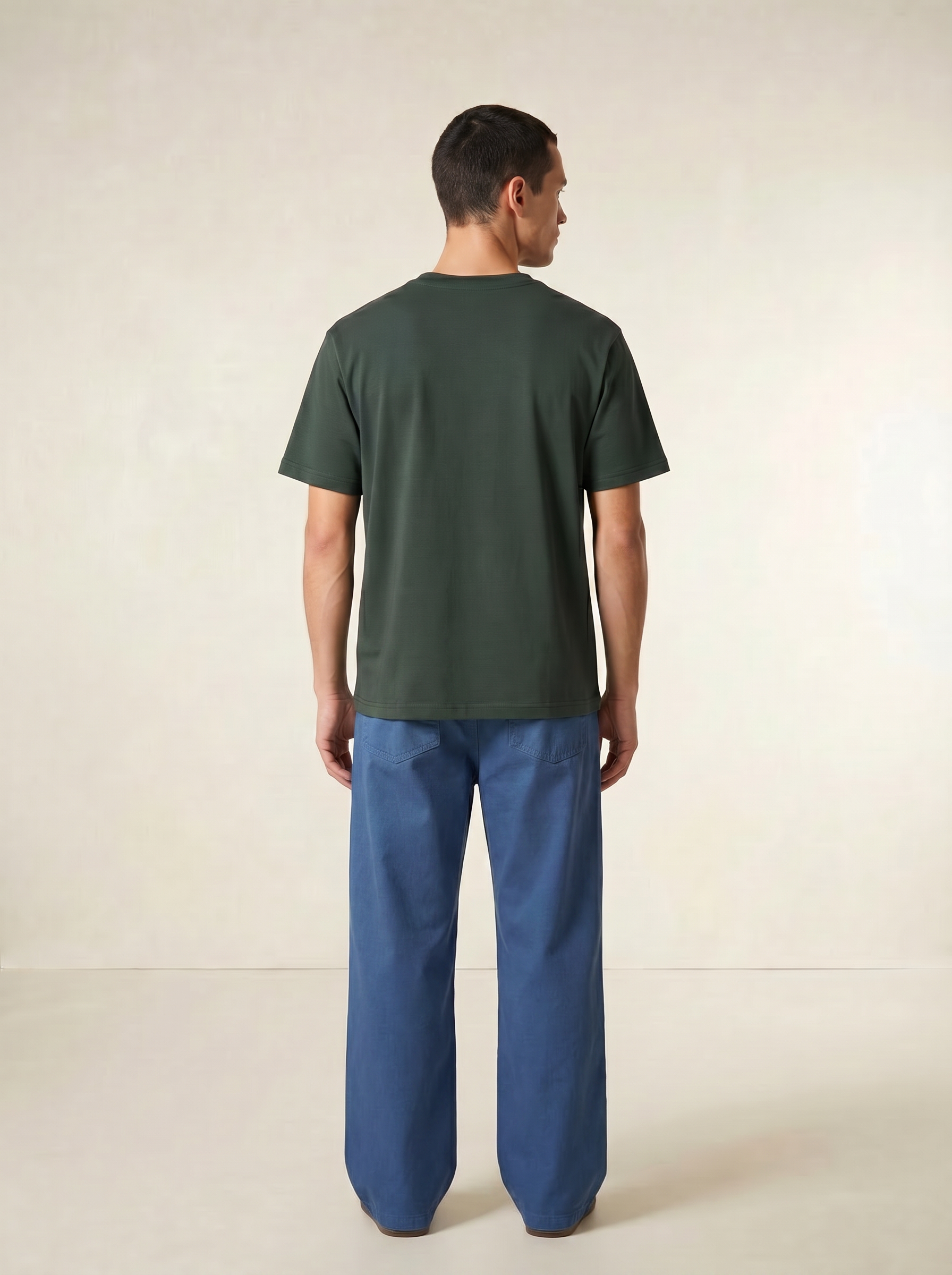 Man wearing a green t-shirt and blue pants on a beige background