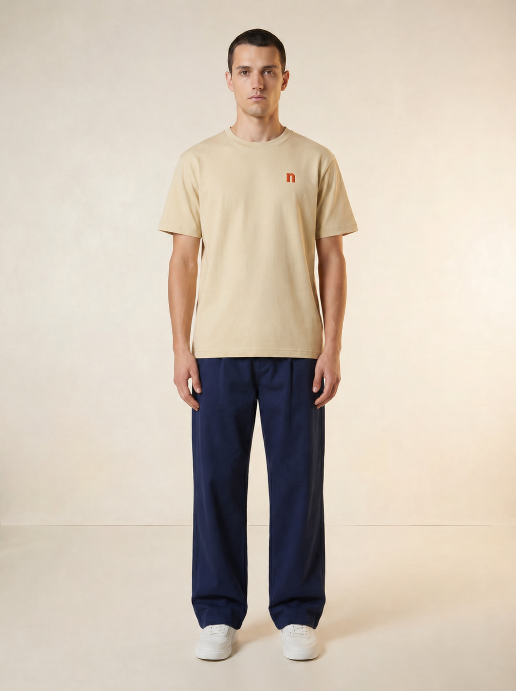 Man wearing a beige t-shirt and navy pants on a plain background