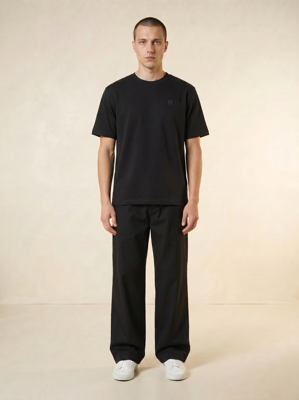 Person wearing a black t-shirt and black pants on a beige background