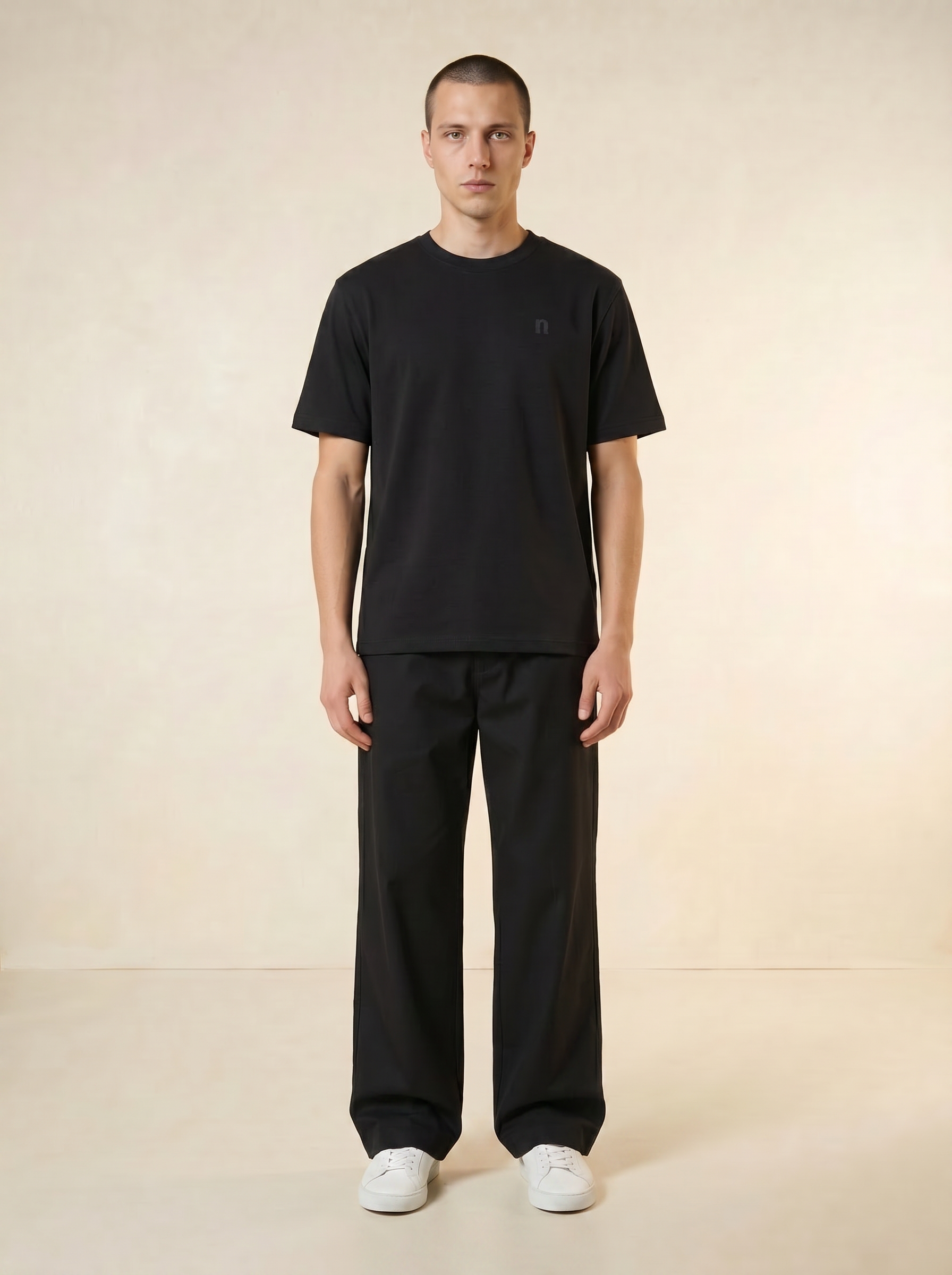 Person wearing a black t-shirt and black pants on a beige background