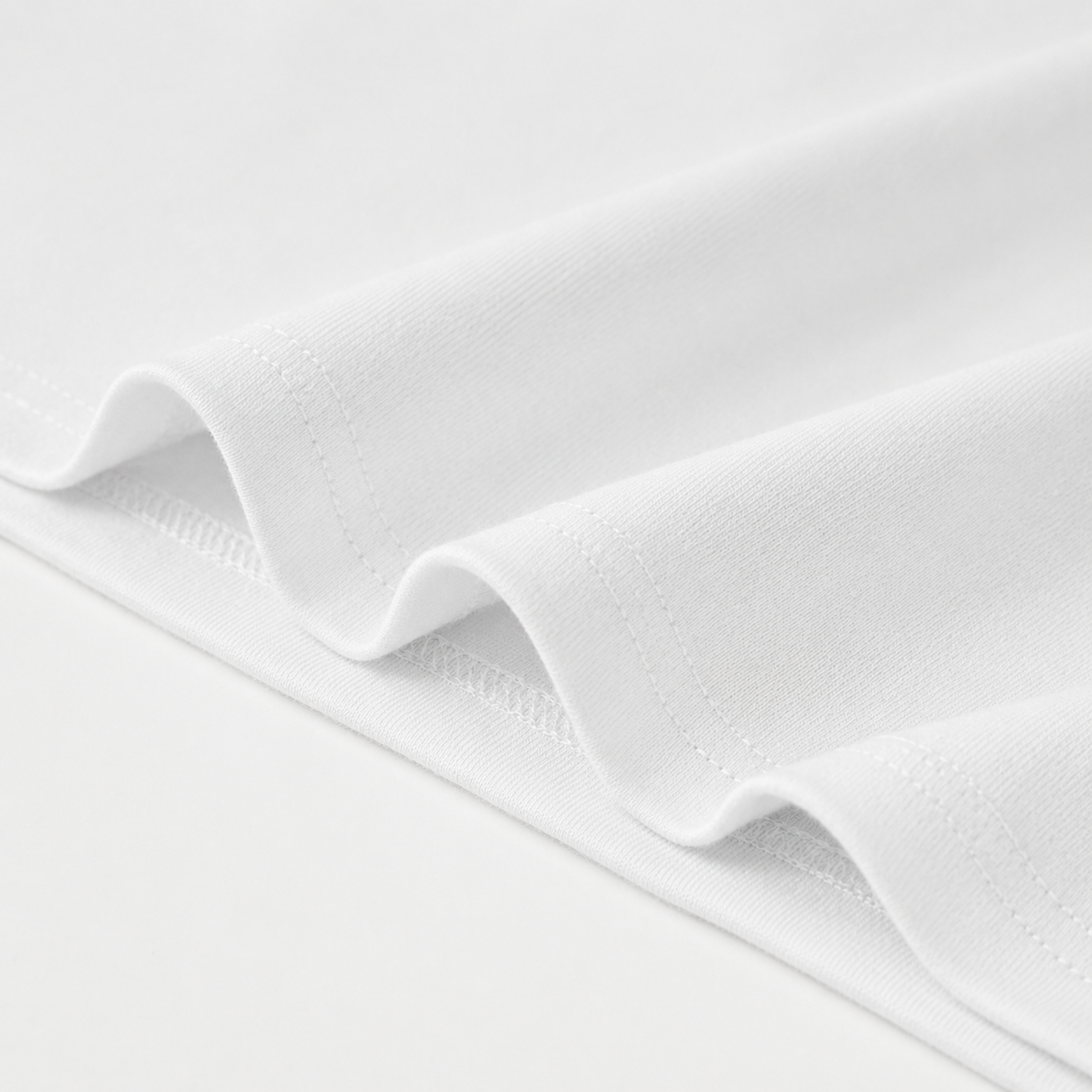 Close-up of white t-shirt bottom edge with a subtle texture on a light gray background