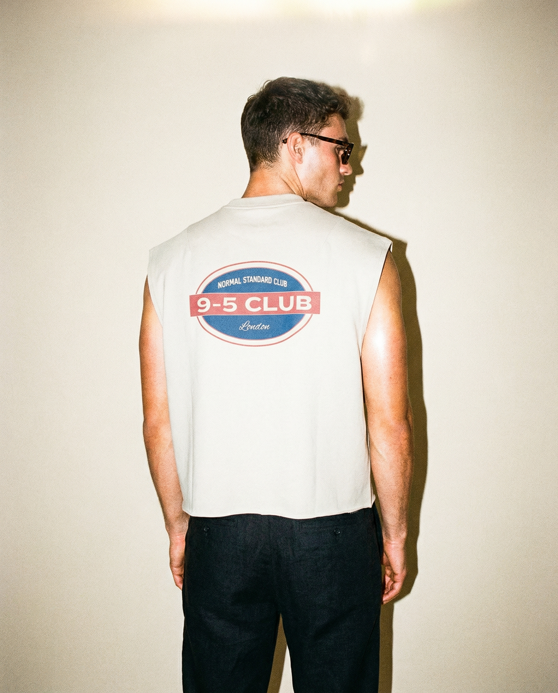 Person wearing a sleeveless shirt with a logo on the back against a plain background