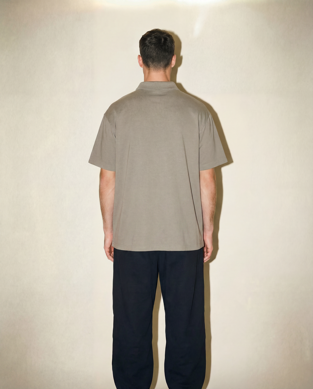 Person wearing a beige shirt and dark pants against a plain background