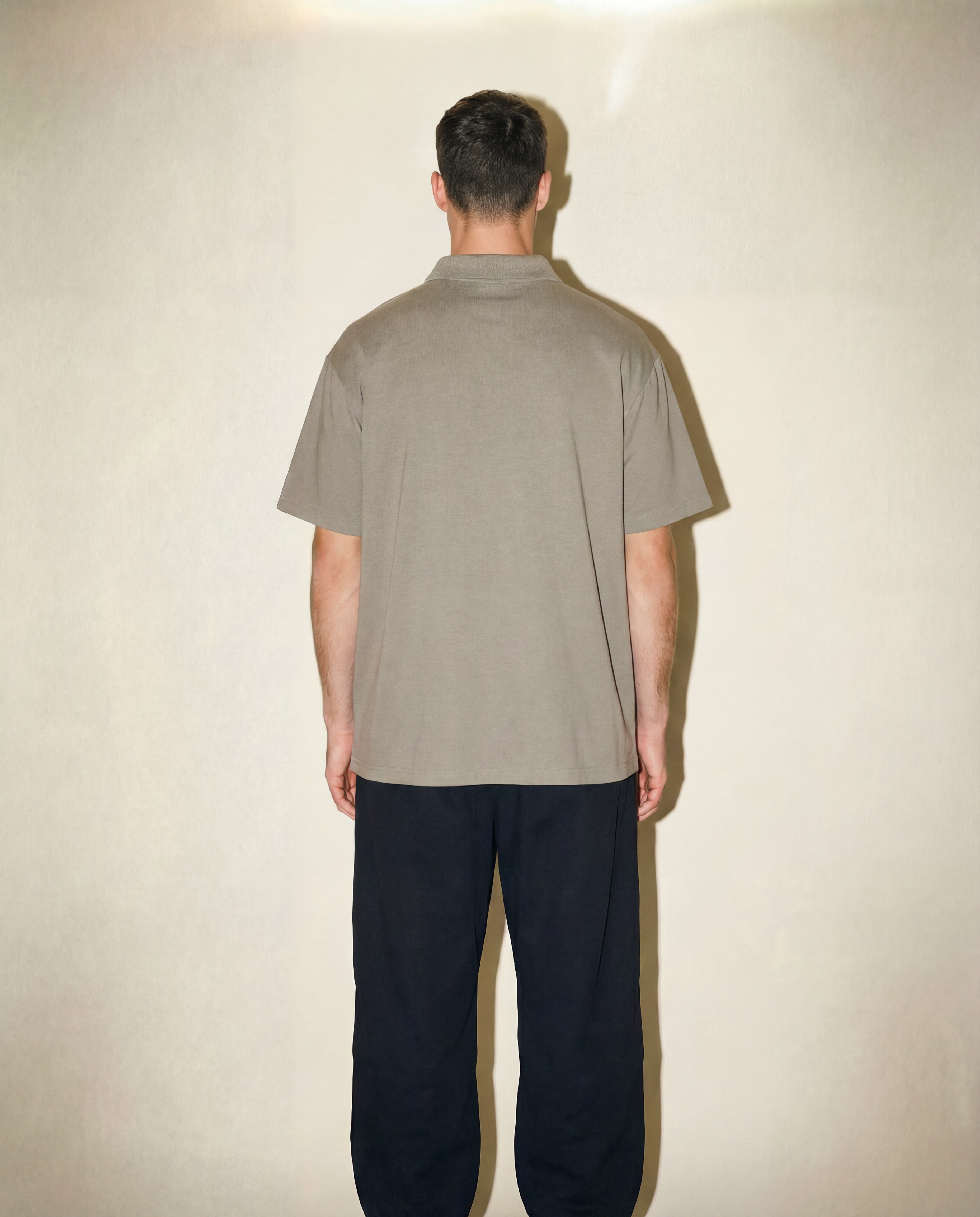 Person wearing a beige shirt and dark pants against a plain background